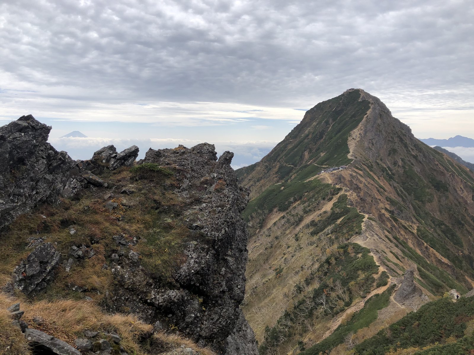 横岳側から振り返った赤岳の尖った山容と、その左奥に小さく見える富士山 南八ヶ岳 ヤマカルテ