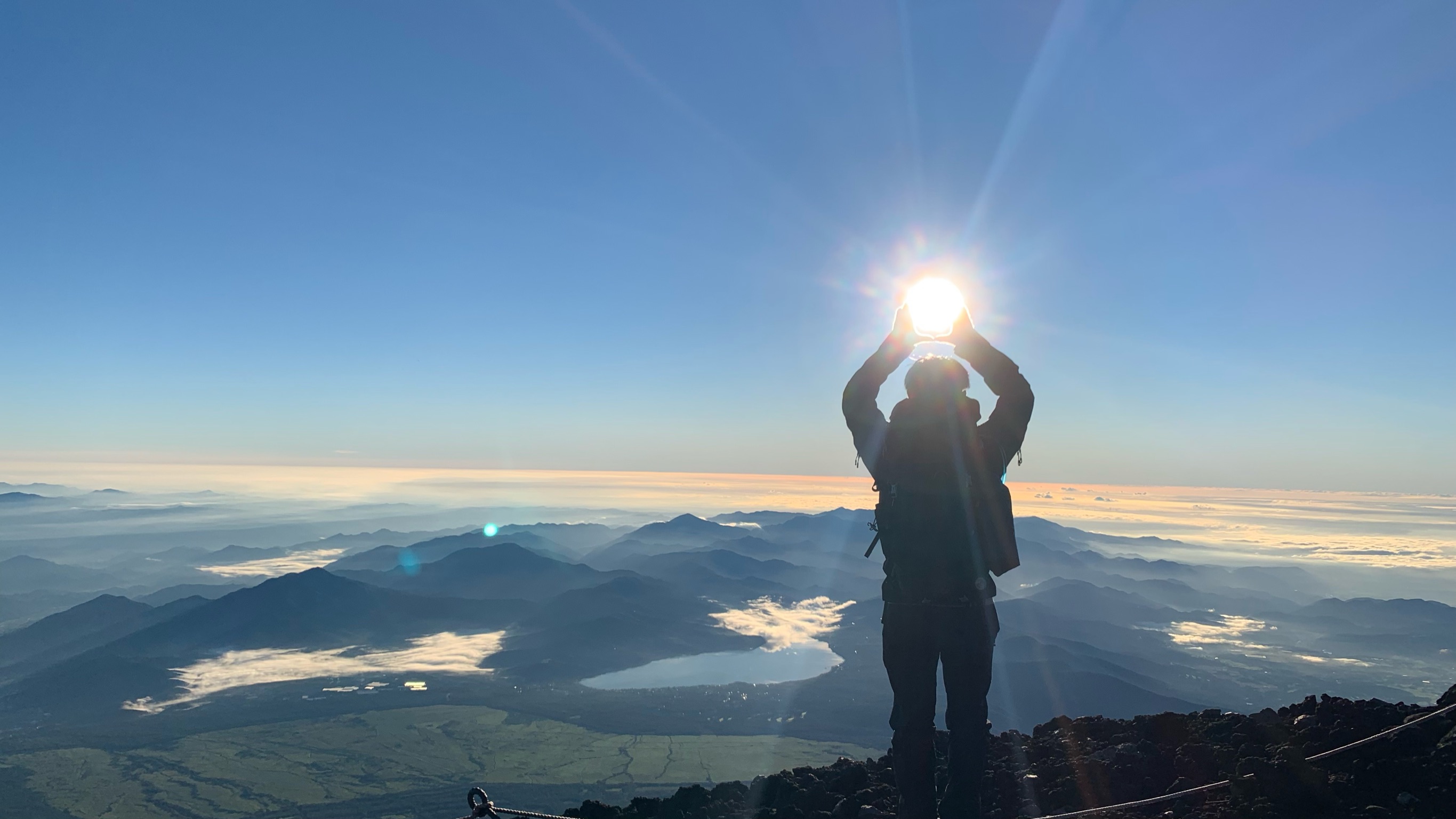 富士山山頂で昇る太陽を掴むポーズの記念写真