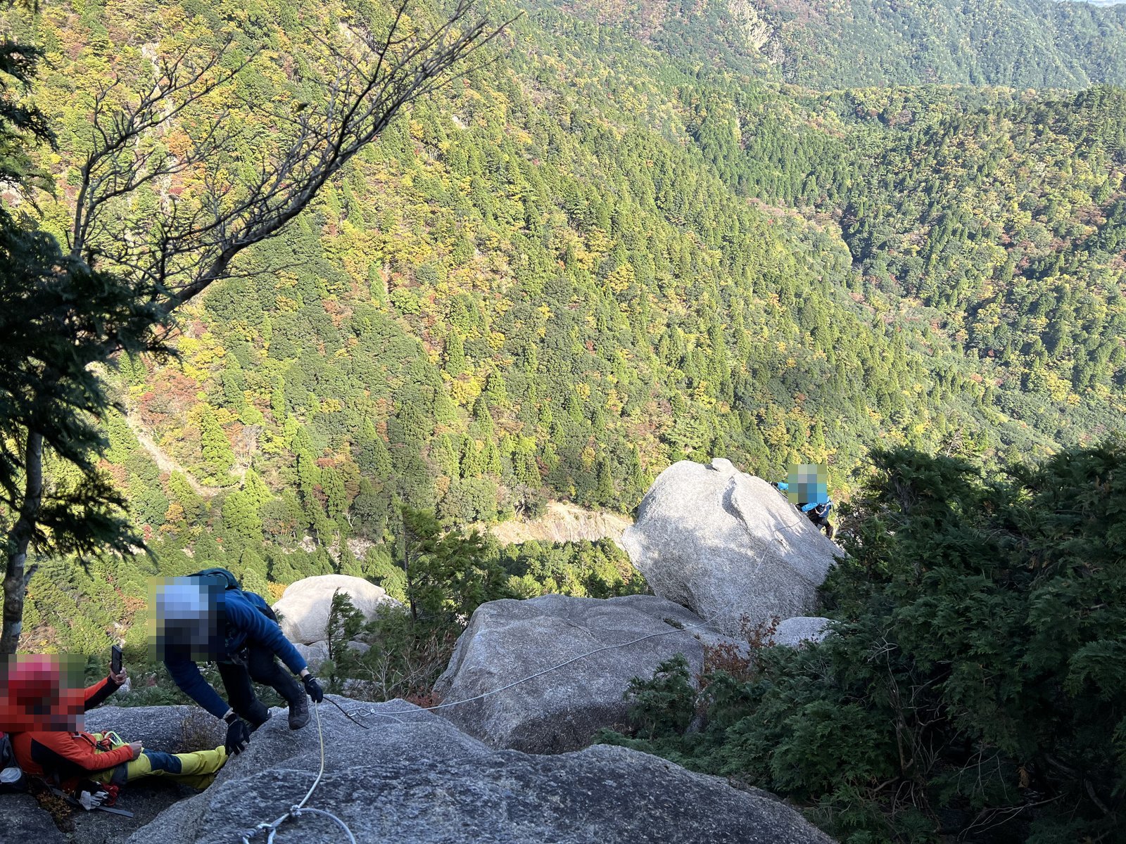 緩い傾斜の岩場で順番に登るメンバーと眼下の紅葉の谷 御在所岳ヴィアフェラータ ヤマカルテ
