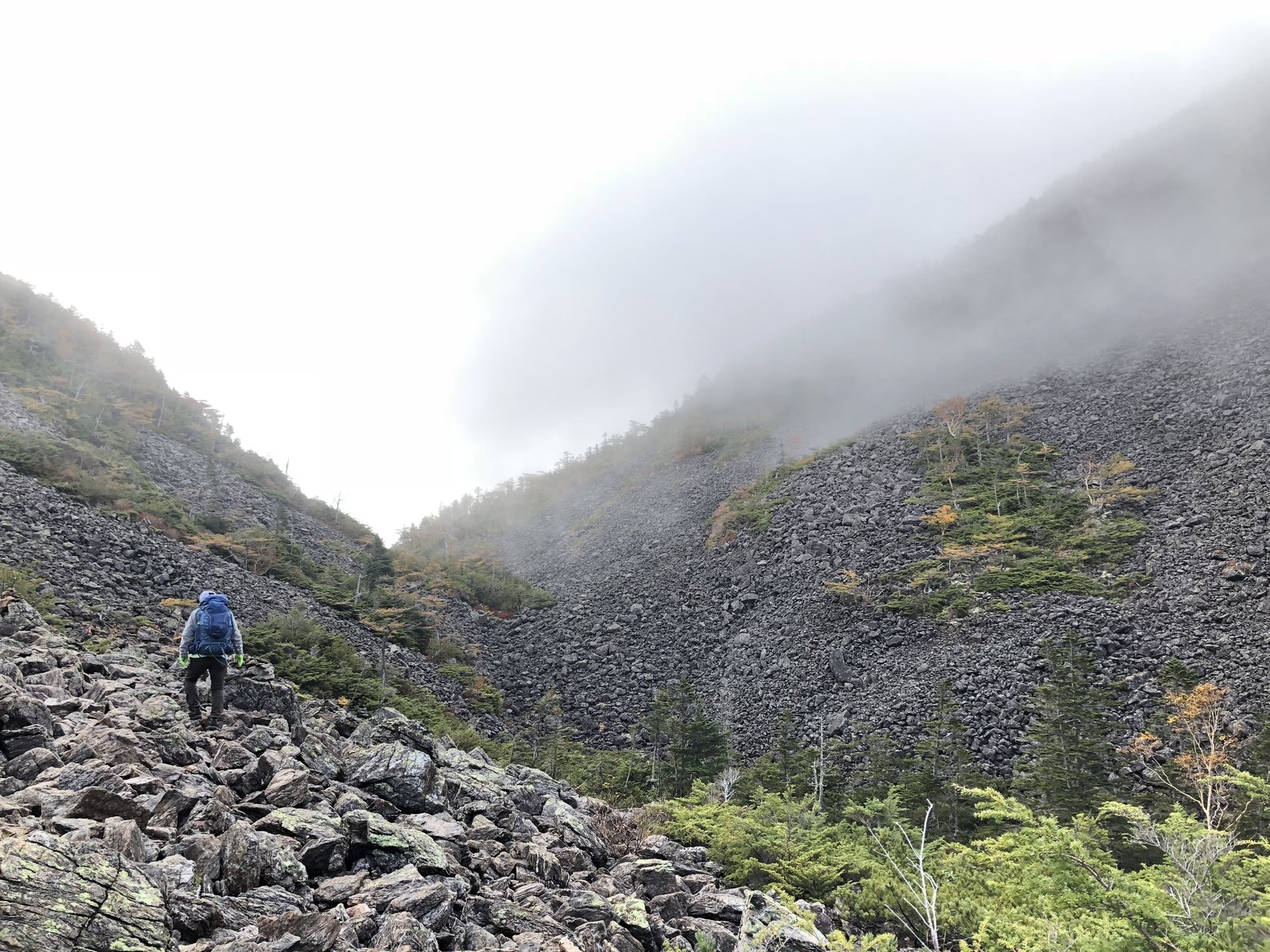 ガスが立ちこめる仙水峠手前のガレ場を登る登山者 甲斐駒ヶ岳