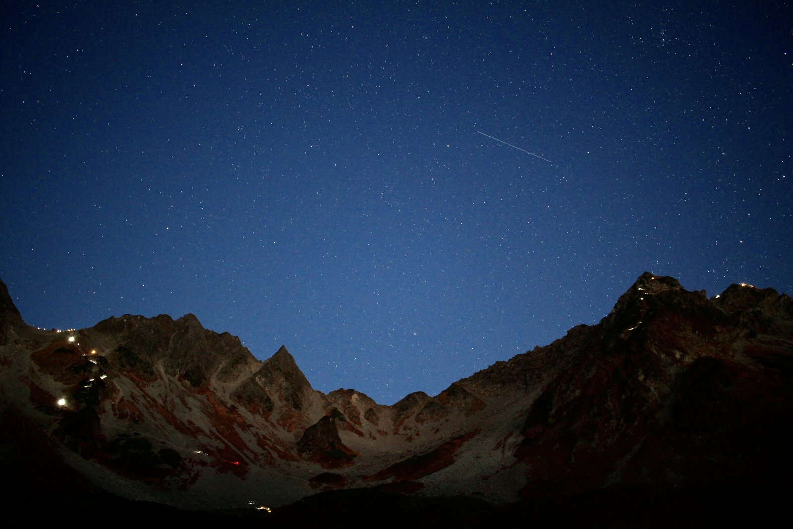 穂高連峰の稜線と星空 早朝に登る登山者のヘッドライトが連なる