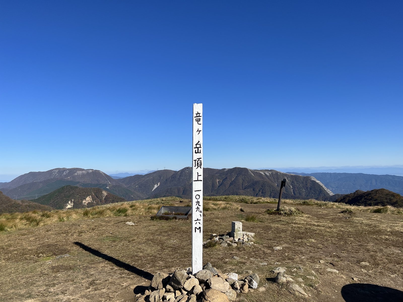 竜ヶ岳の山頂標 標高1099.6m 笹原の山頂と鈴鹿の山並み ヤマカルテ