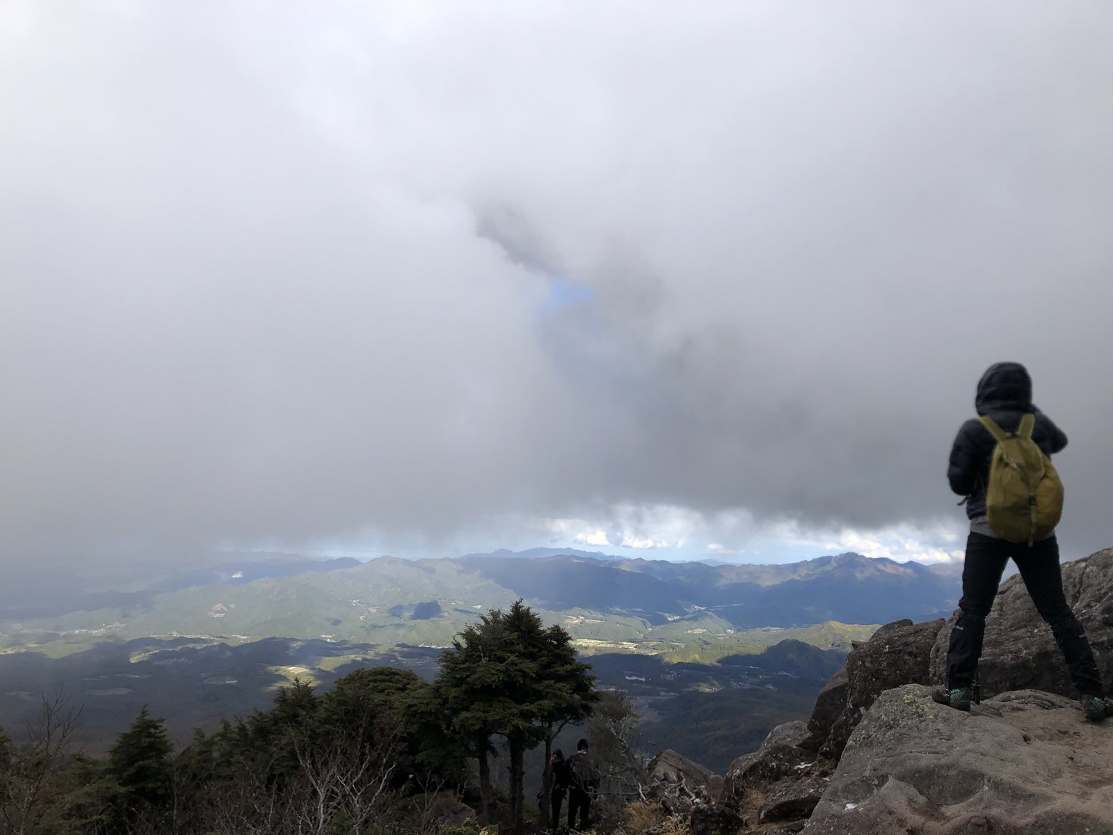 ニュウの岩場から雲の切れ間に見えたふもとの景色と、それを眺める登山者 北八ヶ岳 ヤマカルテ